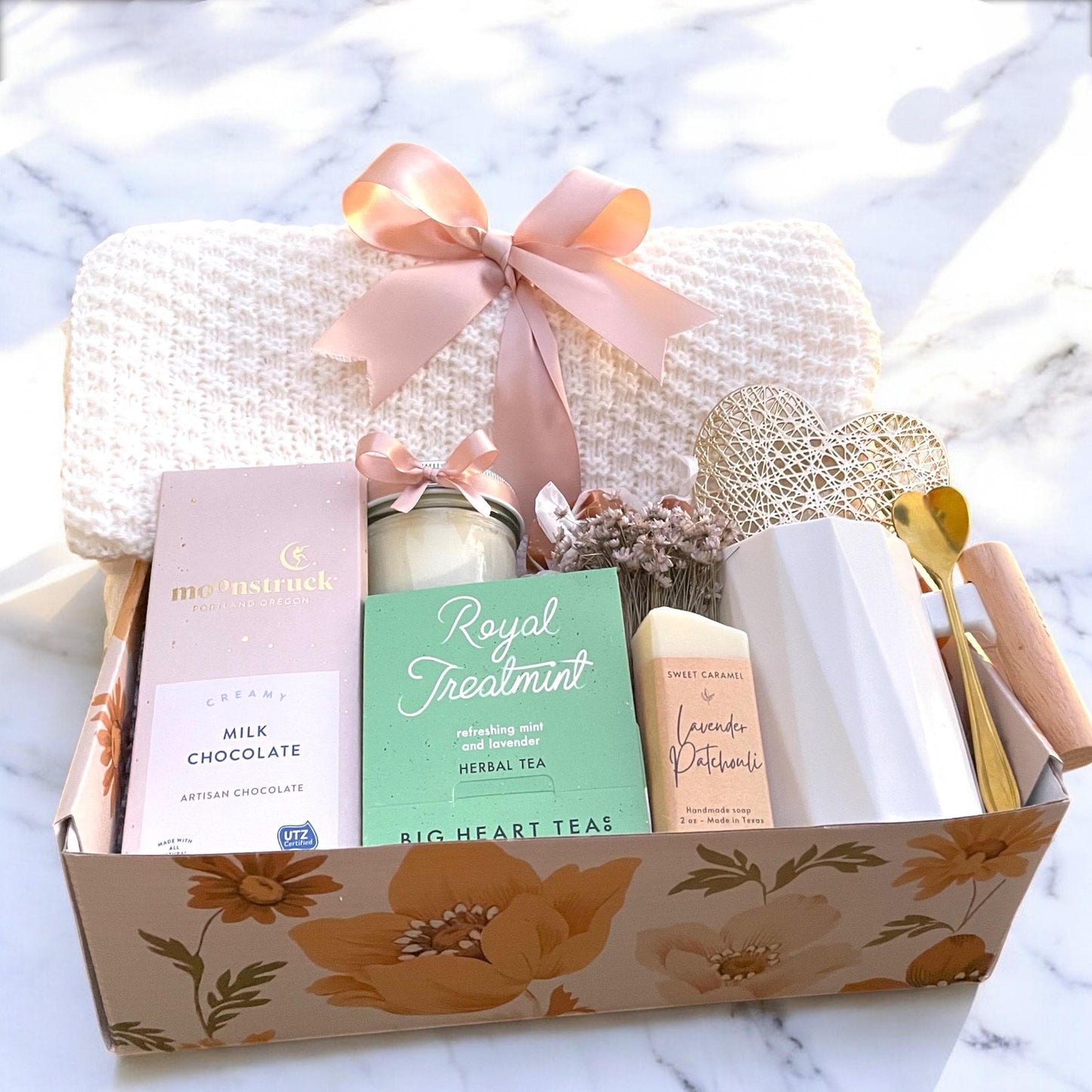 Gift basket with a candle, tea, chocolate, and other items on a marble surface